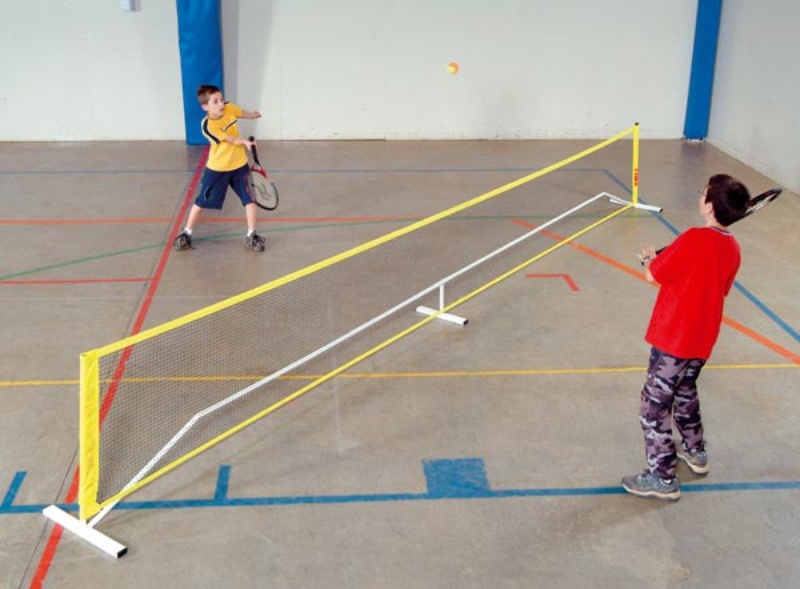 Due bambini giocano a tennis in un palazzetto dello sport con una rete portatile