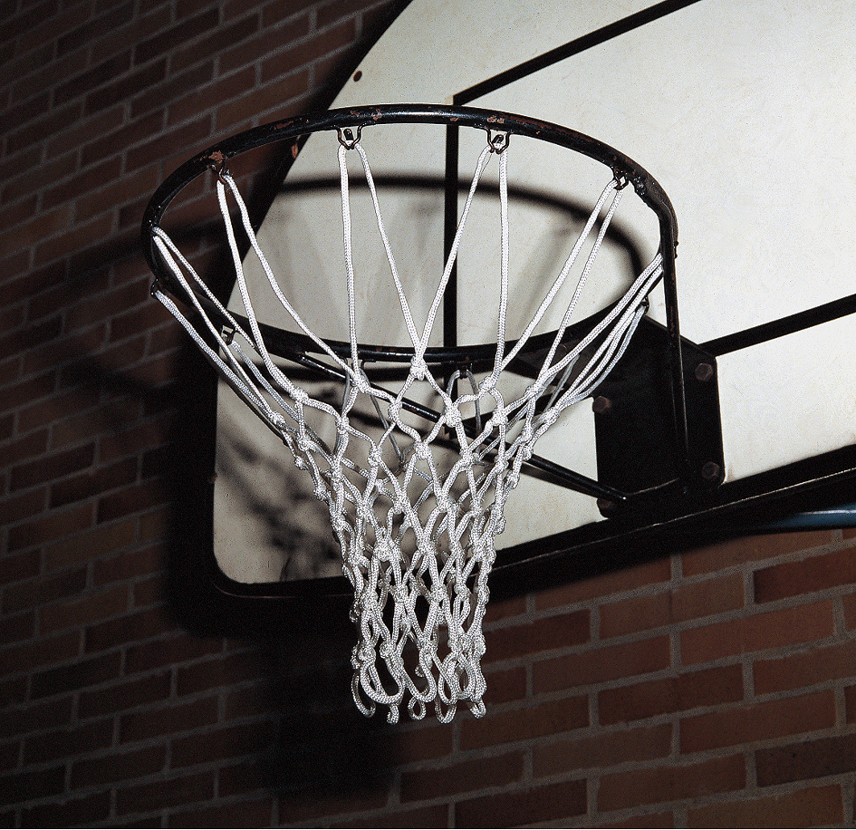 Nahaufnahme eines Basketballkorbs mit Netz, montiert auf einem Backsteinplatz bei Nacht.