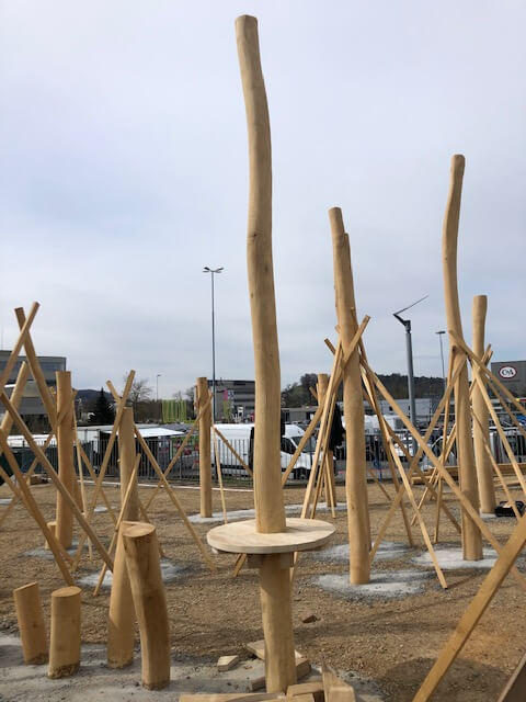 Ein neuer Spielplatz mit hohen Holzstrukturen im Bau, umgeben von einer urbanen Kulisse.