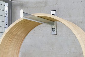 Detailansicht einer modernen Wandhalterung, die eine gebogene Holzkonstruktion an einer Betonwand befestigt