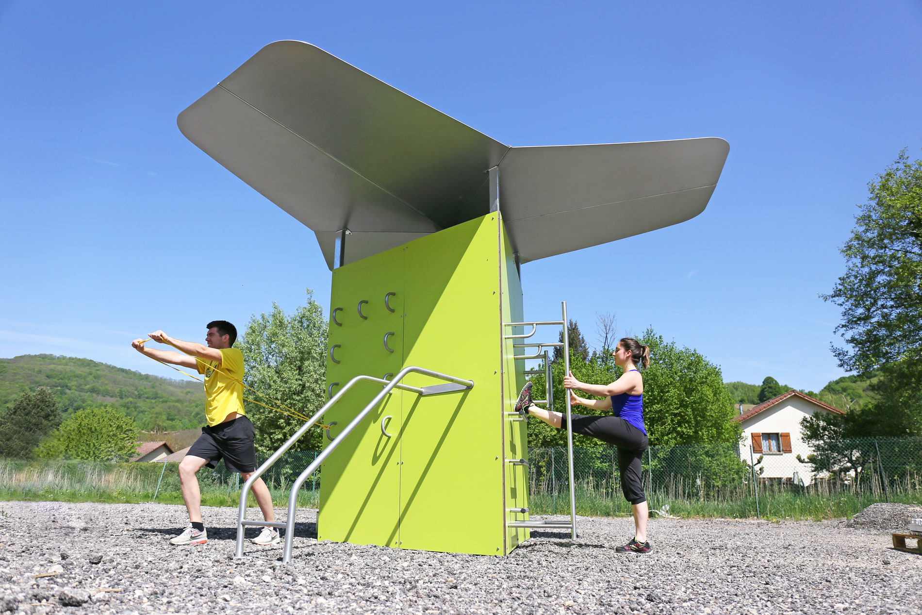 Zwei Personen trainieren im Freien an einem grünen Outdoor-Fitnessgerät bei sonnigem Wetter
