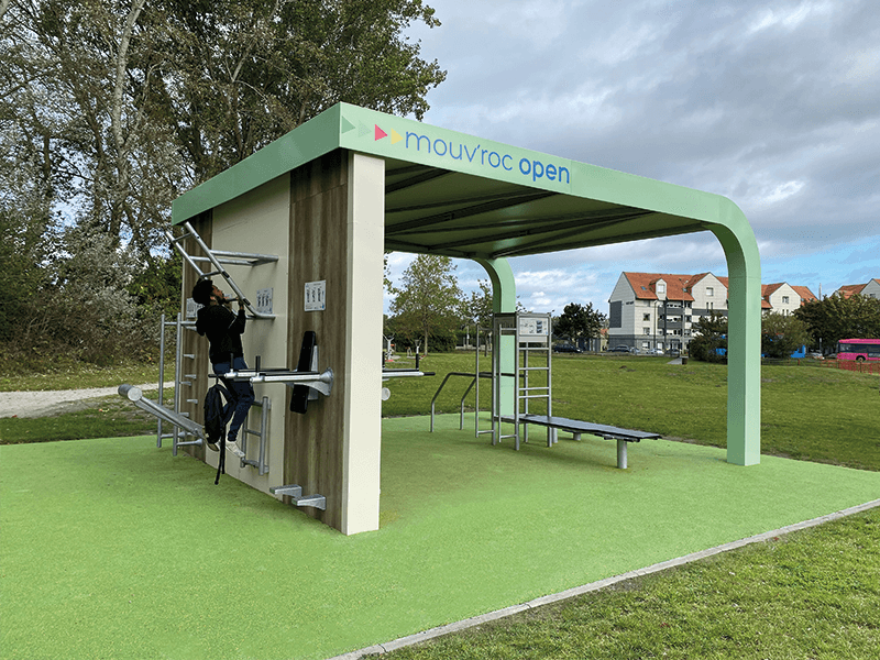Grüner Outdoor-Fitnessplatz mit verschiedenen Trainingsgeräten und einem Sportler, der klettert