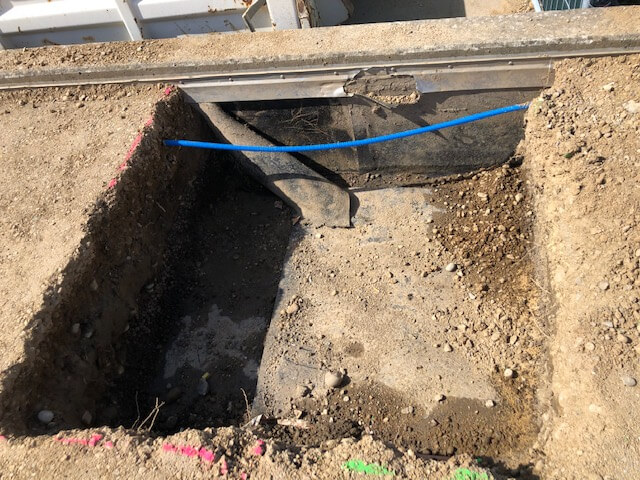 Ein freigelegter Kabelgraben auf einer Baustelle, sichtbar sind Sand, Erde und ein blaues Kabel.