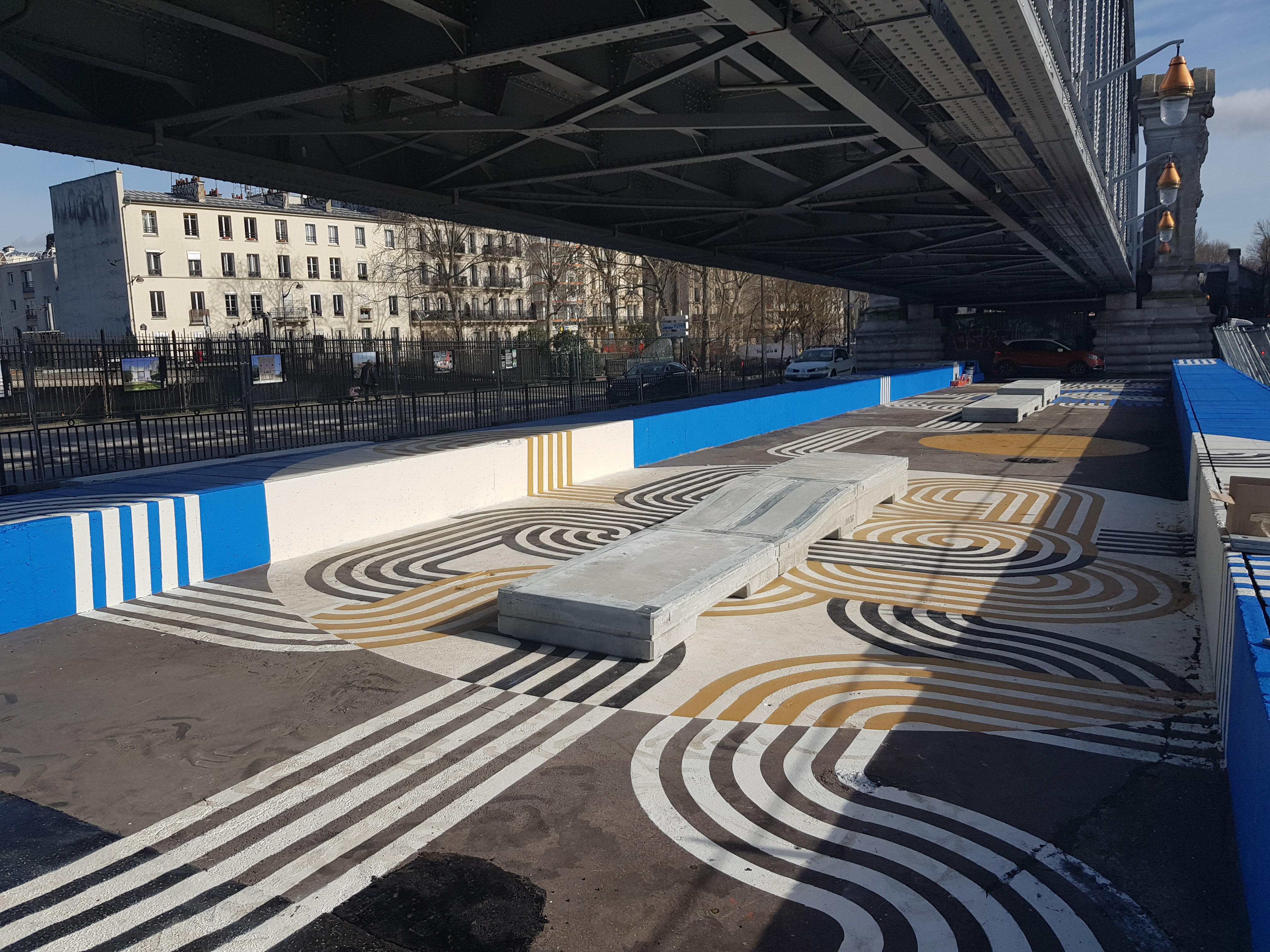 Kunstvolle Straßenmalerei mit geometrischen Mustern in Schwarz, Weiß und Gold unter einer Brücke in städtischer Umgebung.