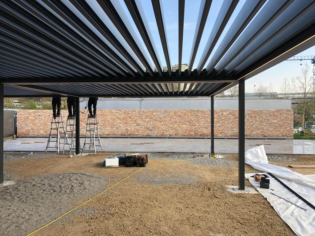 Arbeiter montieren eine Metallüberdachung auf einer Terrasse mit Ziegelwand im Hintergrund
