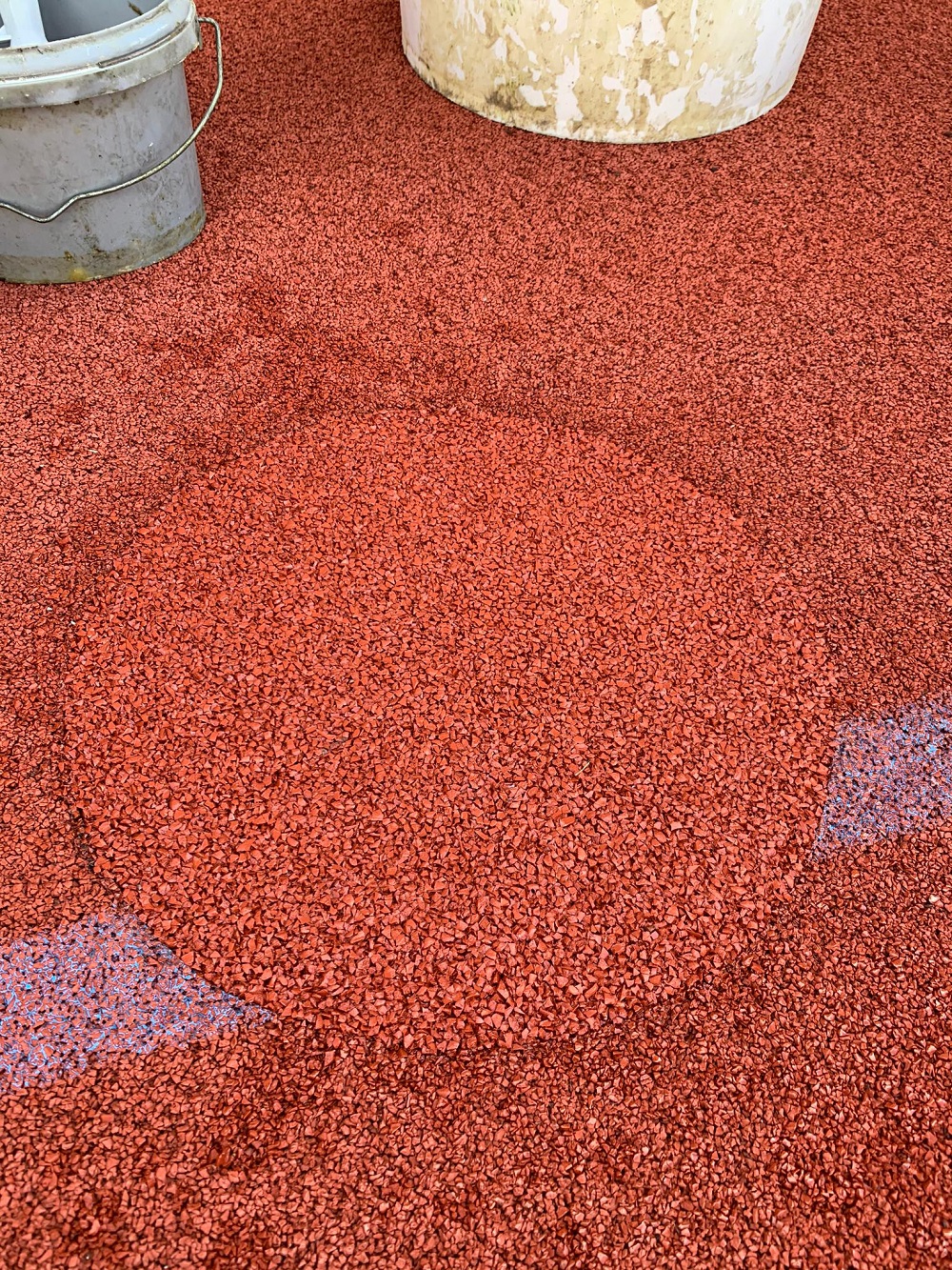 Nahaufnahme eines roten Gummibodenbelags in Installation mit Eimern im Hintergrund