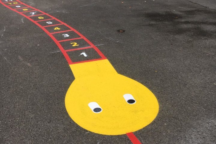 Bunte Spielschlange mit Zahlen von 1 bis 7 bemalt auf einem Asphaltspielplatz.